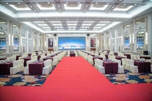 Un salón de conferencias con filas de mesas y sillas, una alfombra roja y una pantalla grande al frente.