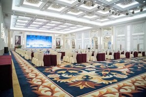 Un salón de conferencias amplio con una larga mesa, sillas blancas y una alfombra estampada.