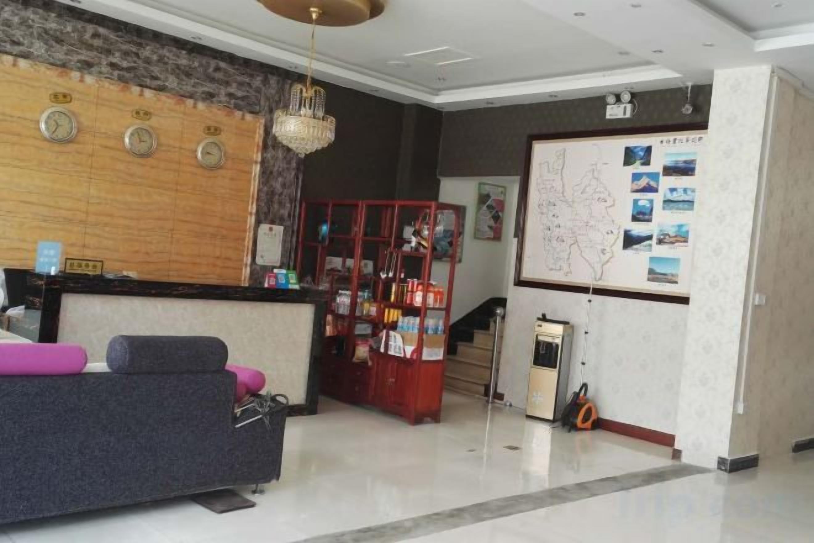A hotel reception area with a reception desk, a seating area with a sofa and chairs, a red display cabinet, and a wall with a map and pictures.