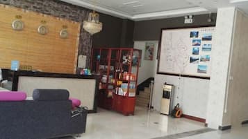 A hotel reception area with a reception desk, a seating area with a sofa and chairs, a red display cabinet, and a wall with a map and pictures.
