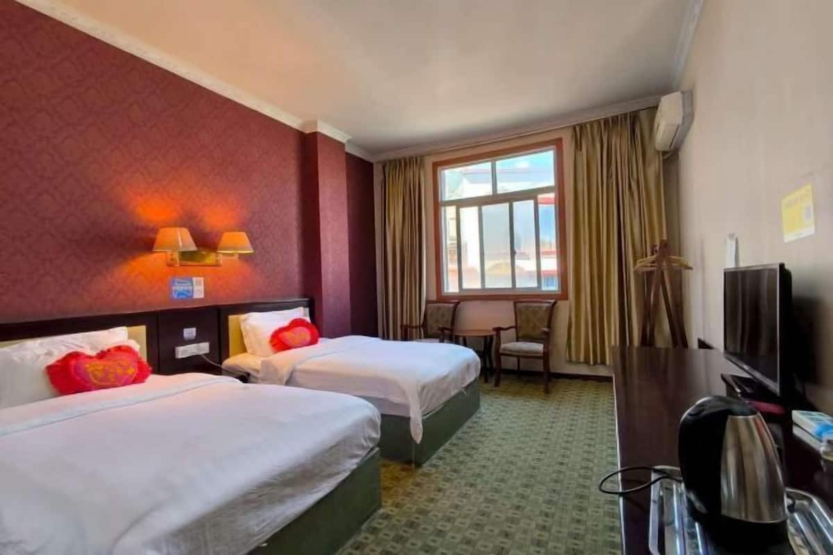 A hotel room with two beds, a desk, a chair, a television, and a window with curtains.