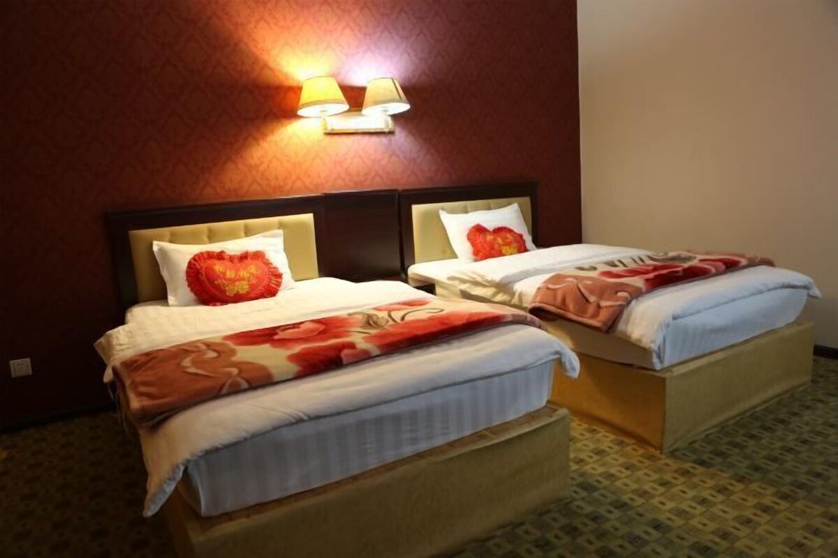 Two beds with headboards, a wall-mounted lamp, and a patterned carpet.
