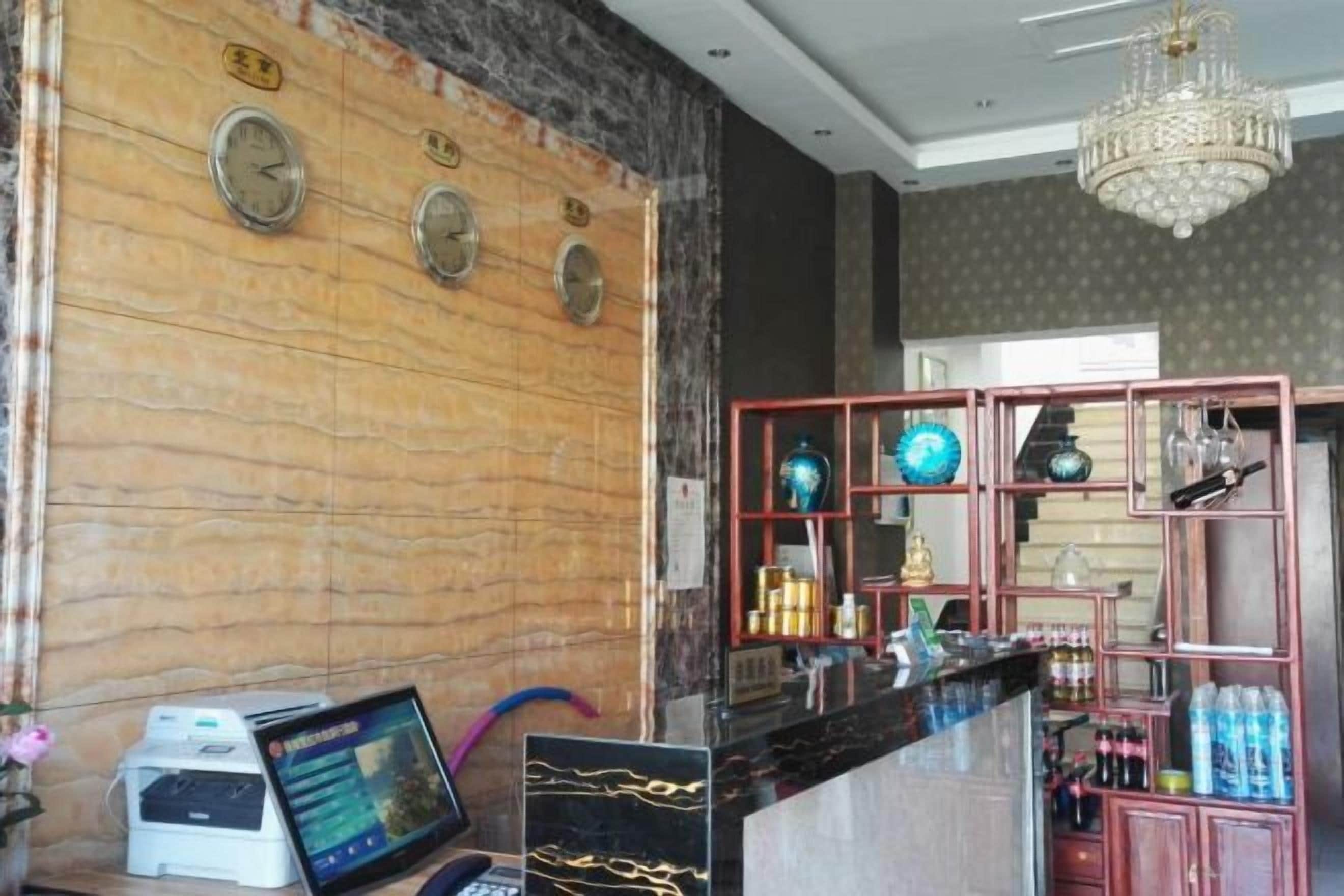 A reception area with a marble wall, clocks, a chandelier, and a bar area with shelves and bottles.
