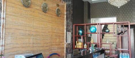 A reception area with a marble wall, clocks, a chandelier, and a bar area with shelves and bottles.