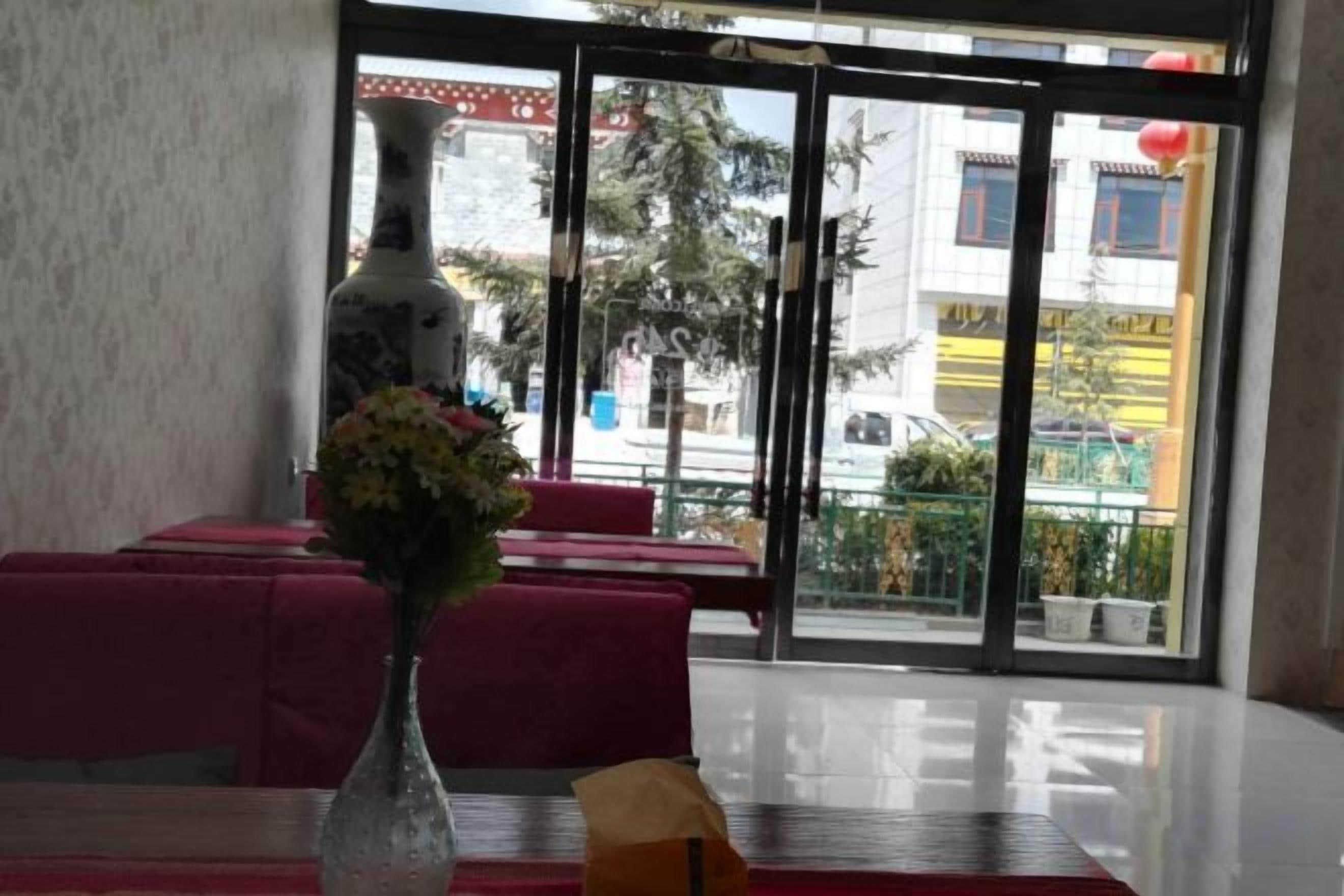A hotel interior with a dining area, a vase with flowers, and a view through the glass doors.