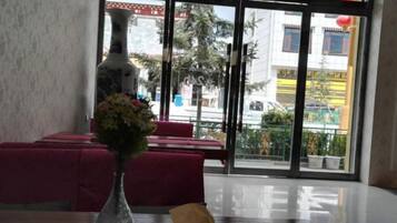 A hotel interior with a dining area, a vase with flowers, and a view through the glass doors.