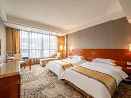 Quarto de hotel com duas camas, uma escrivaninha, uma cadeira e uma janela grande.