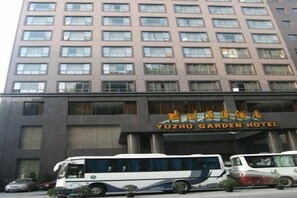 A multi-story building with a sign for YUZHU GARDEN HOTEL. There are several vehicles parked in front, including a bus and a car.