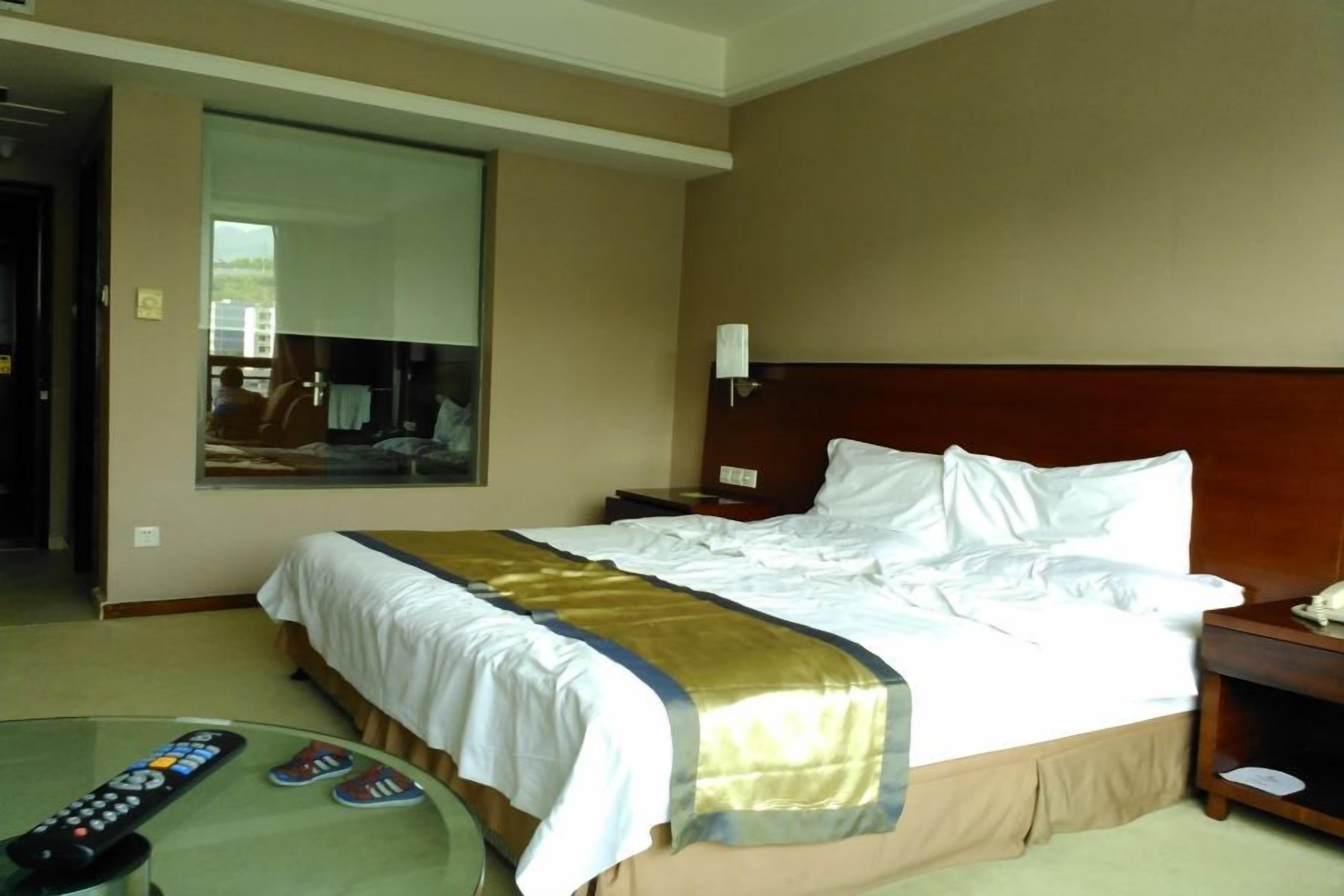 Habitación de hotel con cama, mesita de noche y una mesa de vidrio con un control remoto y pantuflas.