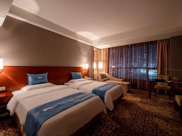 A hotel room with two beds, a sofa, a desk, and a large window with curtains.