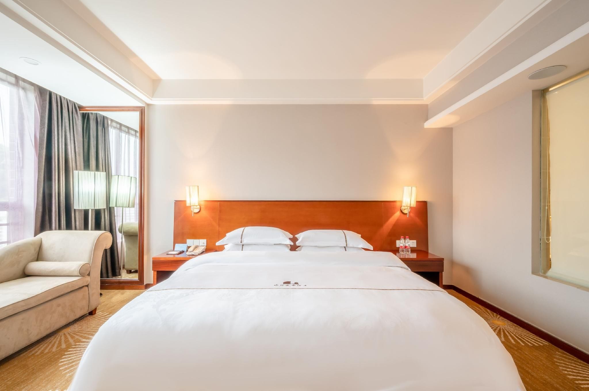 Habitación de hotel con una cama grande, dos mesitas de noche, una silla y una lámpara.