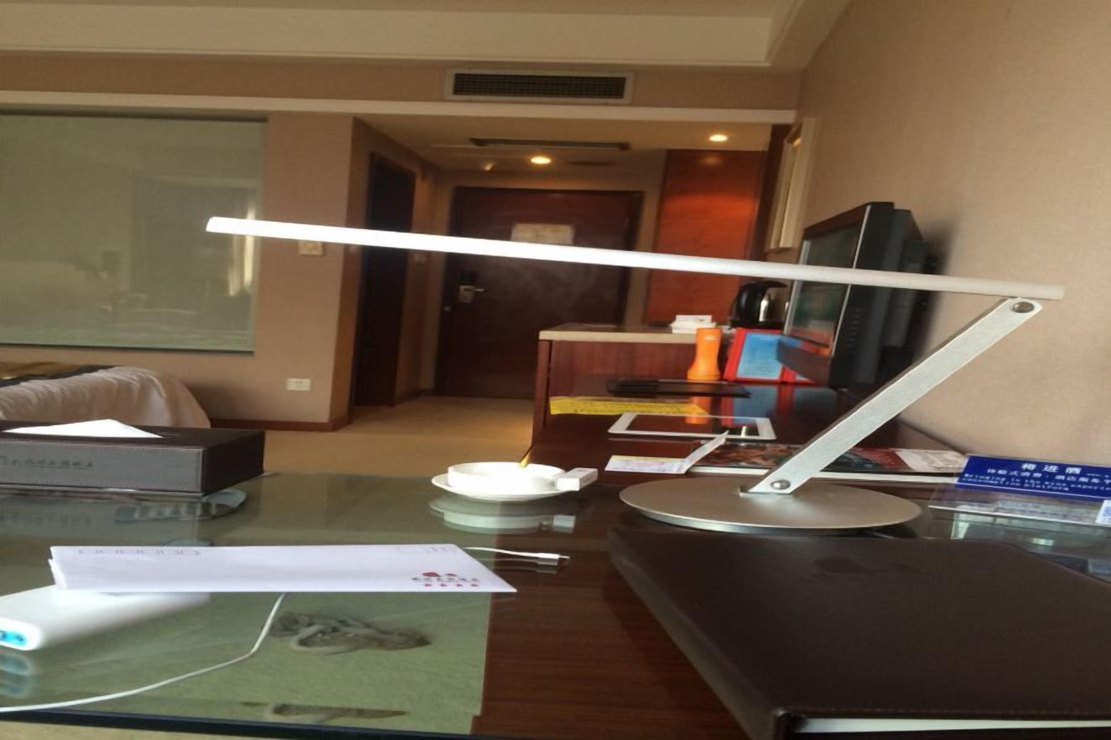 A hotel room with a desk, a television, a lamp, and a bed.