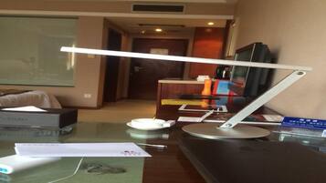 A hotel room with a desk, a television, a lamp, and a bed.