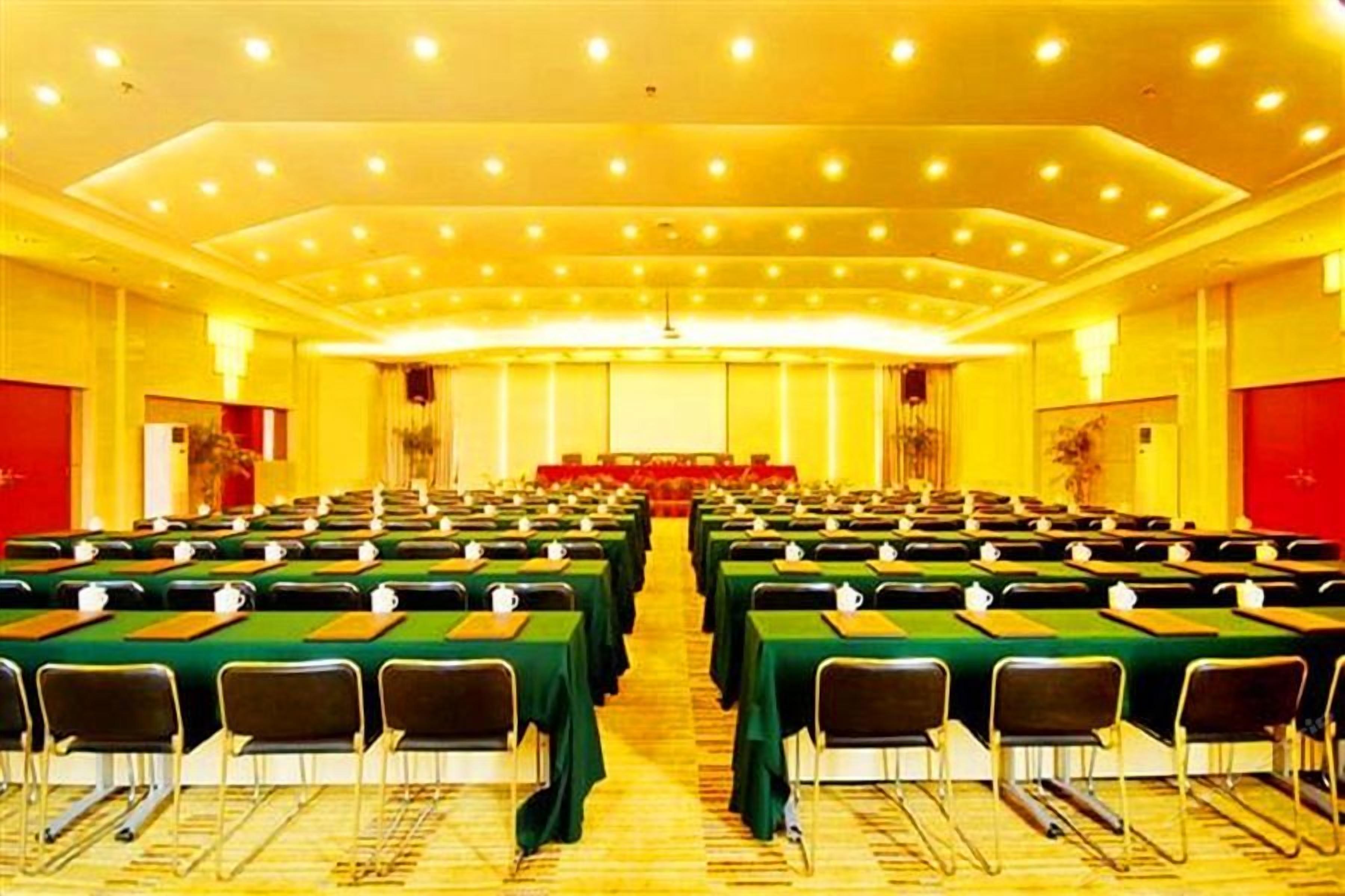 A conference room with rows of tables and chairs, a stage at the front, and a red accent wall.
