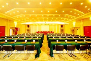 A conference room with rows of tables and chairs, a stage at the front, and a red accent wall.