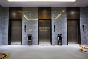 A modern elevator area with marble walls, two elevators, and a floor with a simple geometric pattern.