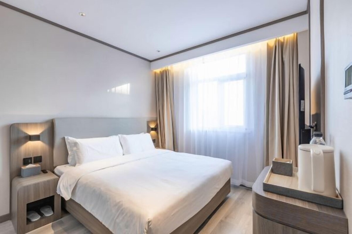 Ein modernes Hotelzimmer mit einem großen Bett, Nachttischen, einem Spiegel und einem Fenster mit Vorhängen.