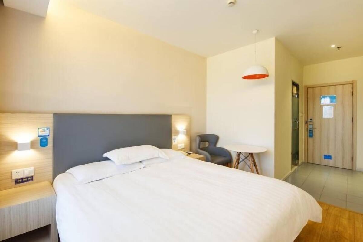 Una habitación de hotel con cama, mesita de noche, lámpara, silla y una pequeña mesa.