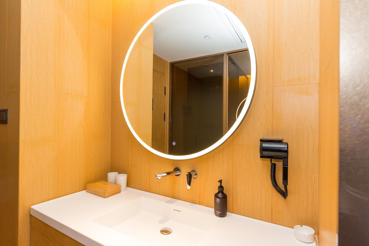 A bathroom with a round mirror, a white sink, a soap dispenser, and a towel warmer.