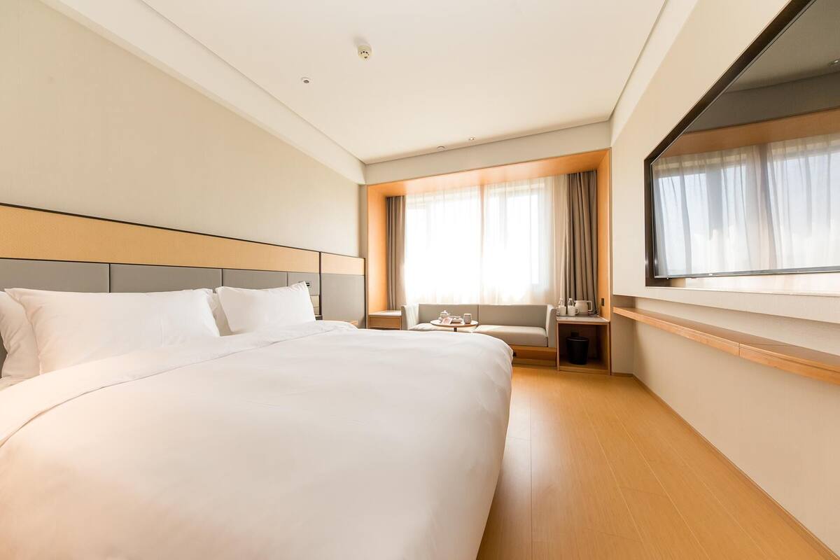 Habitación de hotel con una cama grande, zona de estar con mesa y televisor fijado a la pared.