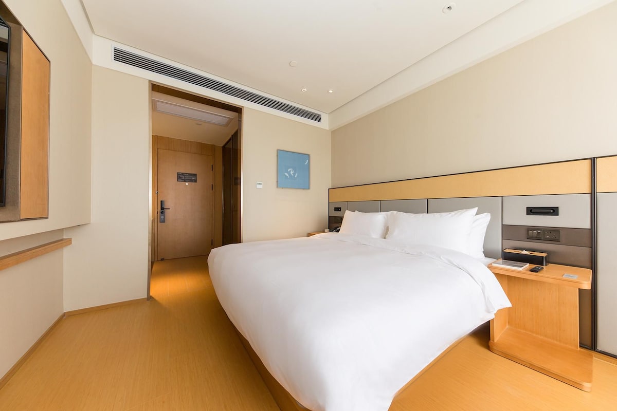 A hotel room with a bed, bedside table, and a door leading to another room.