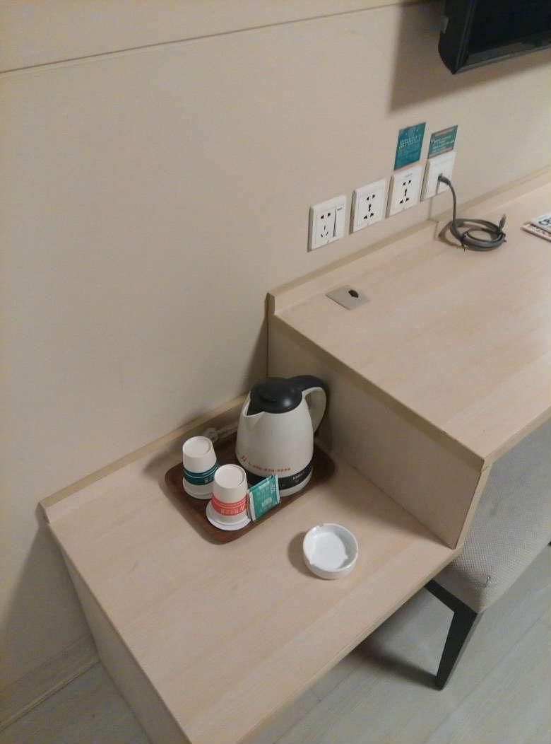A hotel room with a wooden desk, a kettle, and a tray with cups and a saucer.