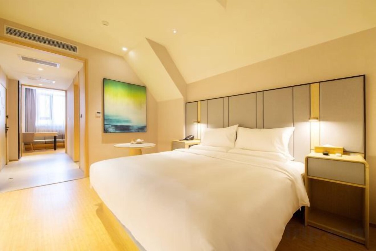 A hotel room with a large bed, bedside tables, a painting on the wall, and a view of the hallway.