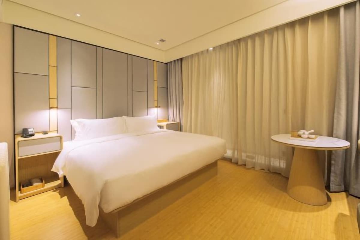 A hotel room with a large bed, bedside tables, a round table, and a curtain.
