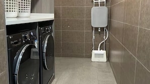 A compact laundry room with two front-loading washing machines, a white water dispenser, and a shelf with white baskets. - Hanting Express Zhongshaner Road (Guangzhou)