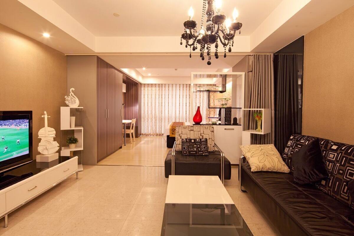 A modern living room with a flat-screen TV, a coffee table, a sofa, and a chandelier.