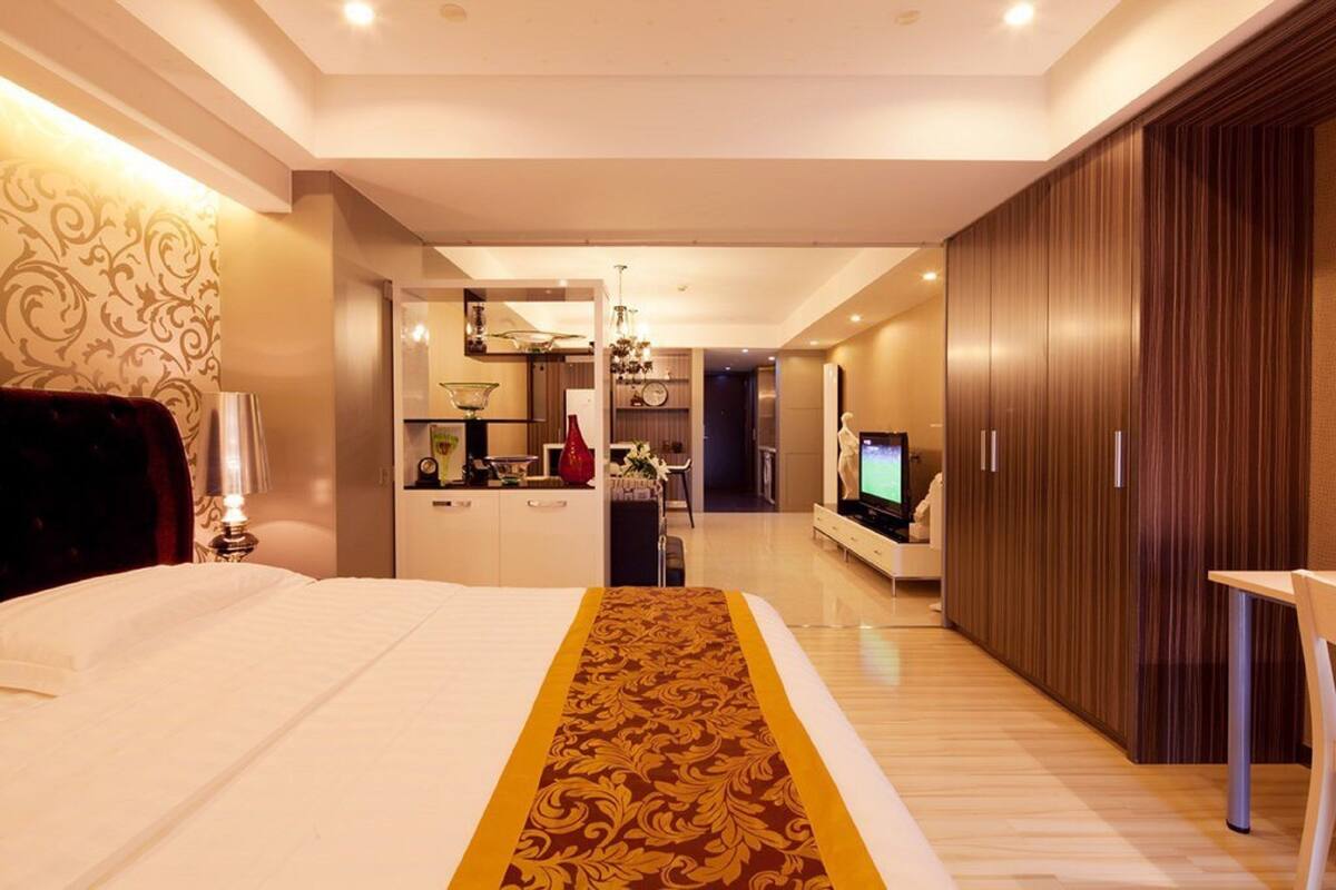 A modern hotel room with a large bed, a TV, a wardrobe, and a dining area.