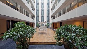 A modern atrium with a central wooden platform, surrounded by potted plants and glass railings. - Wangfujing Xin Xiang Ya Yuan Apartment (Beijing)