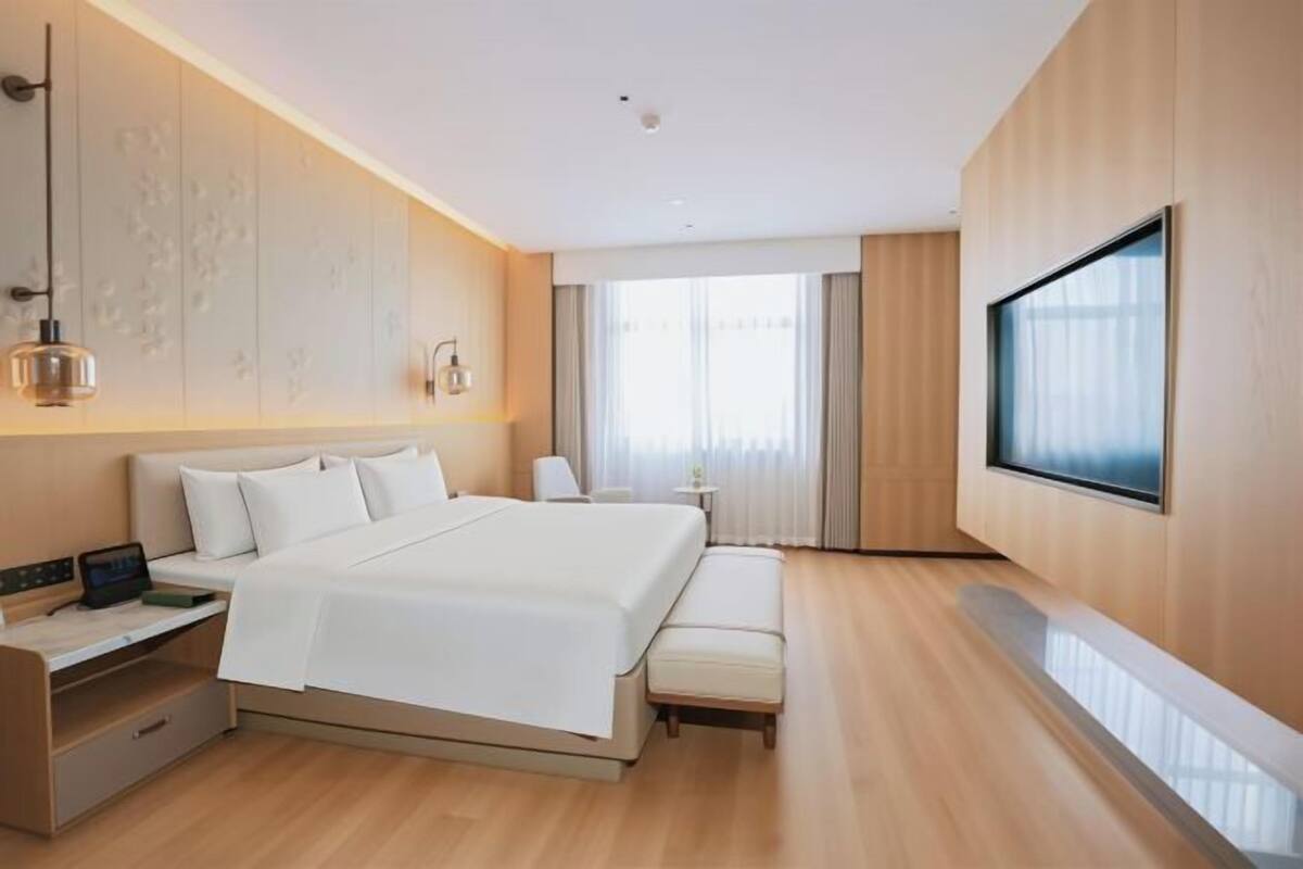 Una habitación de hotel moderna con una cama grande, mesitas de noche, un escritorio y un televisor.