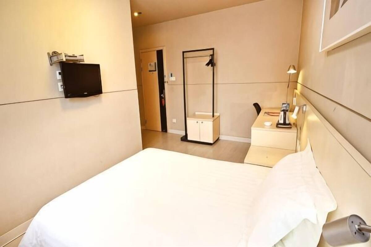 A hotel room with a bed, a bedside table with a lamp, a mirror, and a TV.