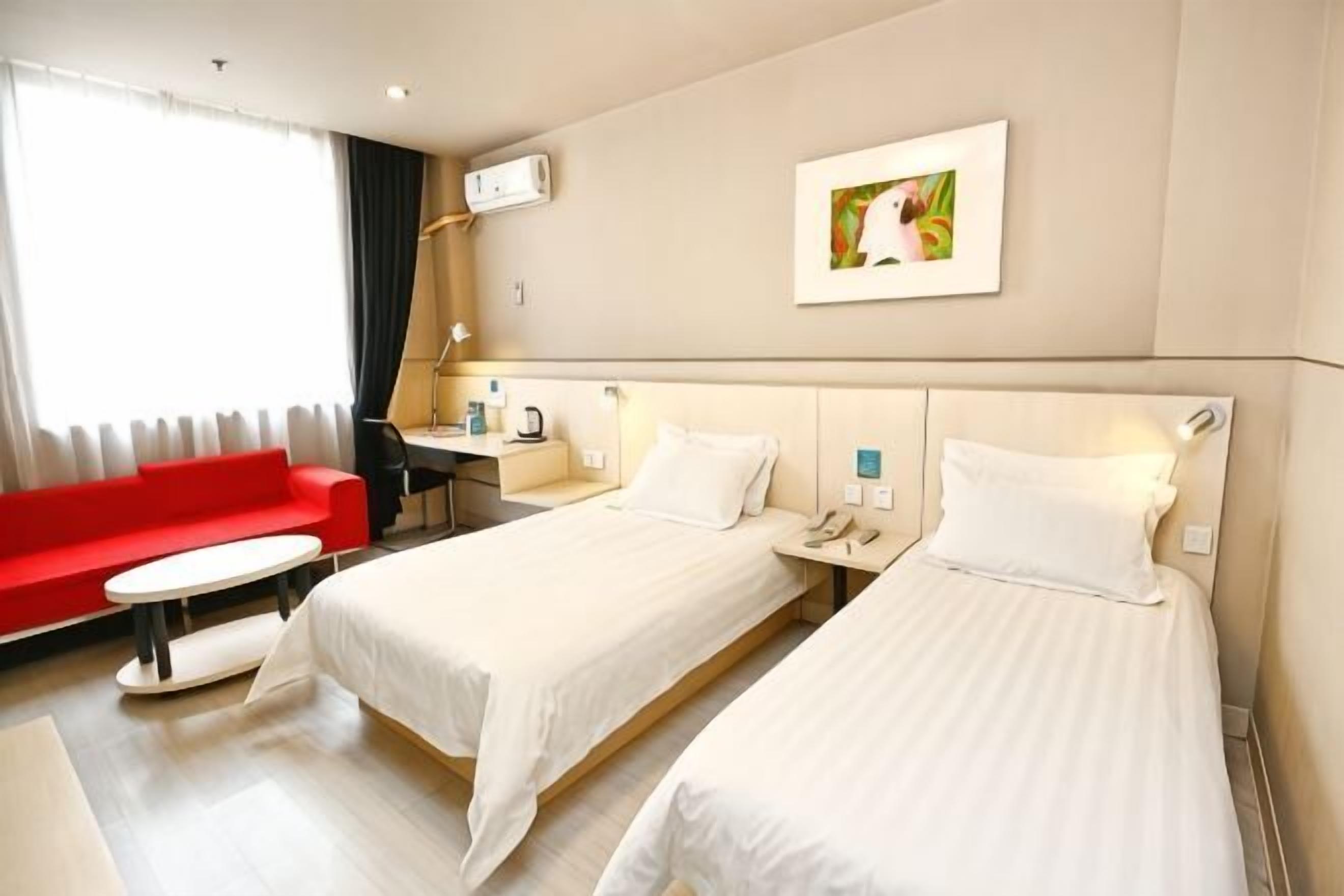 Ein Hotelzimmer mit zwei Betten, einem roten Sofa, einem Schreibtisch und einem Fenster mit Vorhängen.