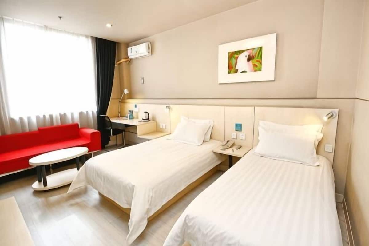 A hotel room with two beds, a red sofa, a desk, and a window with curtains.