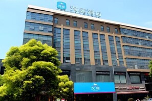 A multi-story hotel with a modern facade, featuring a prominent sign at the top and several ground-level shops. - HanTing Hotel (Nantong Jinfeida Plaza) (Nantong)