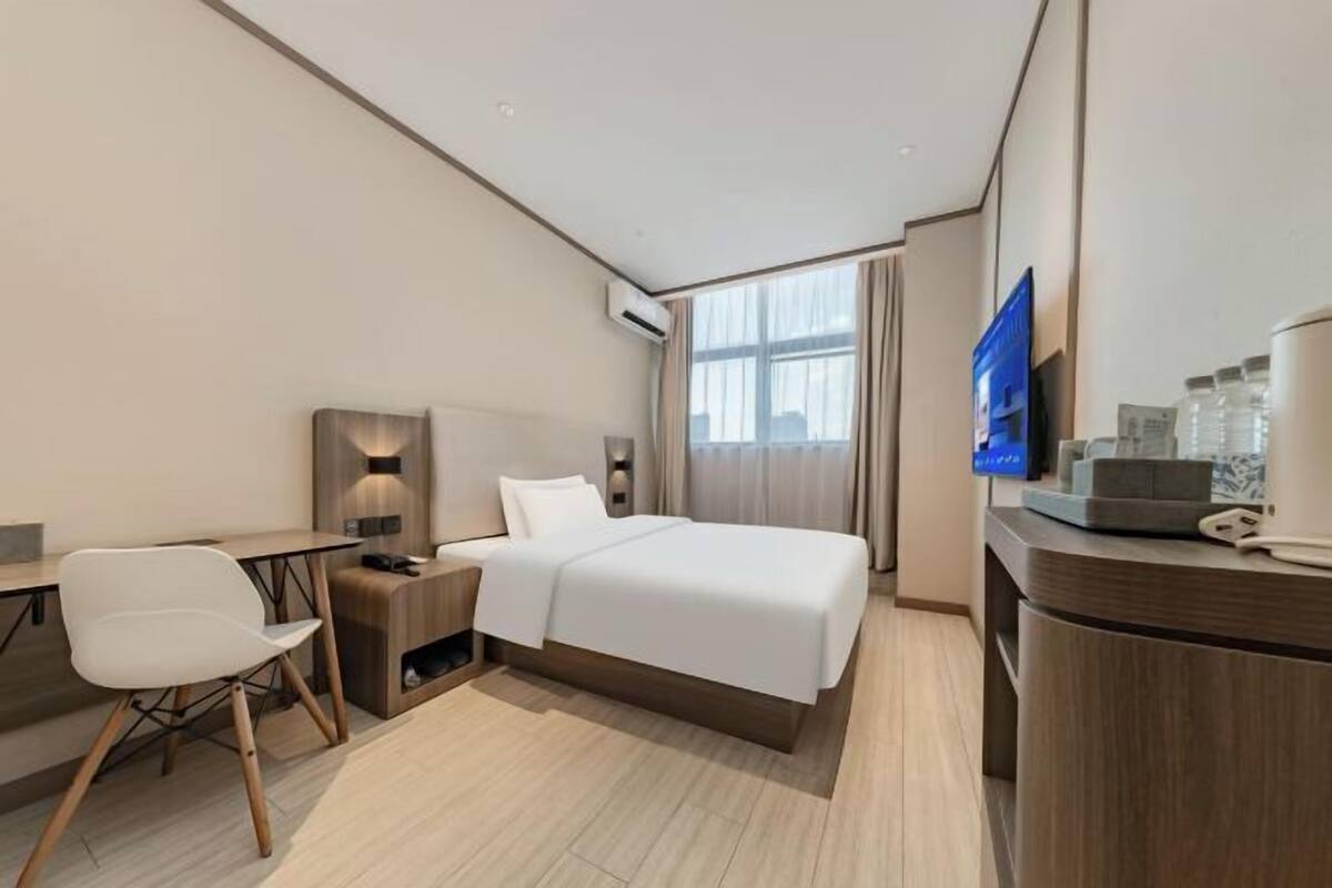 A hotel room with a bed, a desk, a chair, a TV, and a minibar.