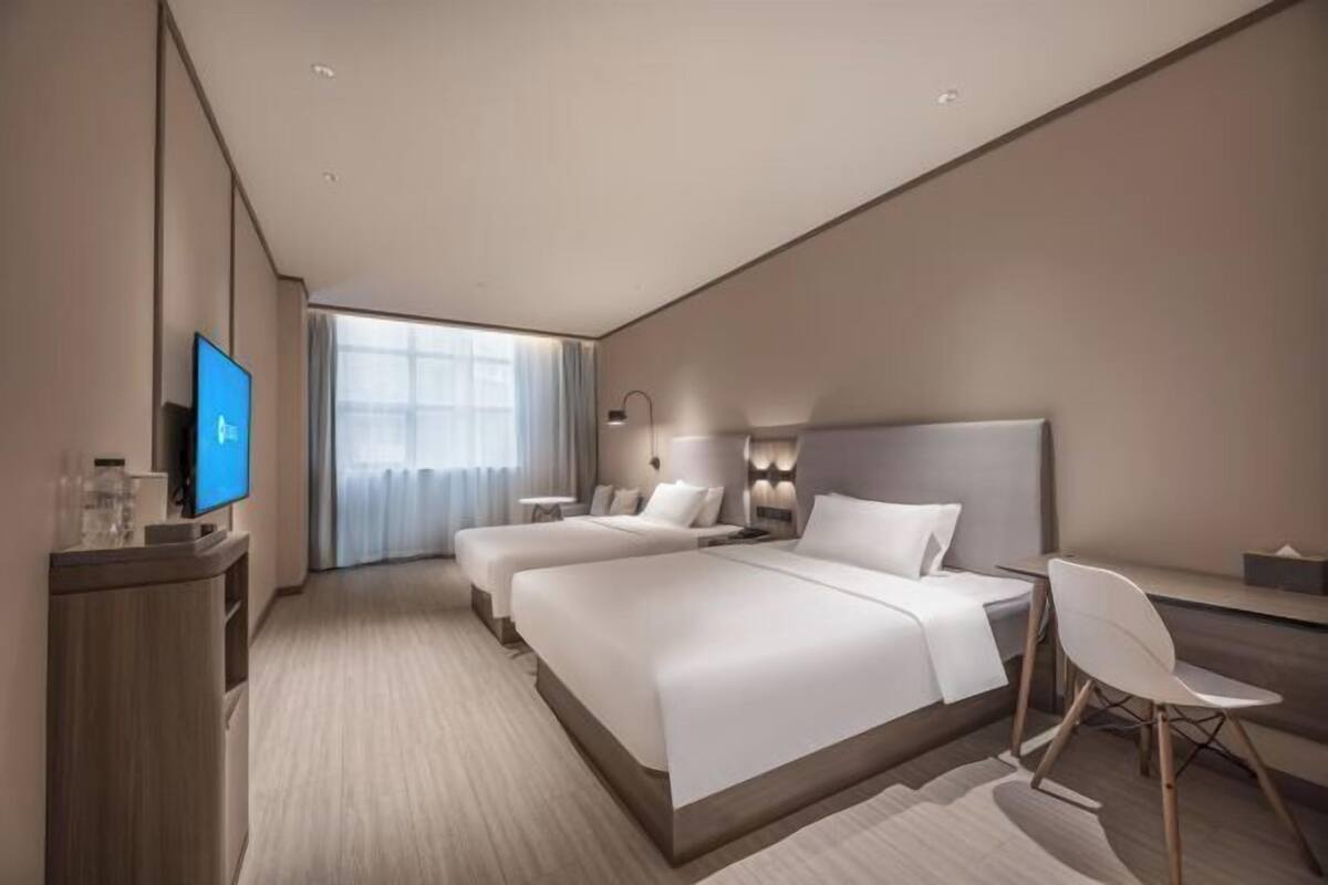 A modern hotel room with a large bed, a desk, a chair, a TV, and a window with curtains.