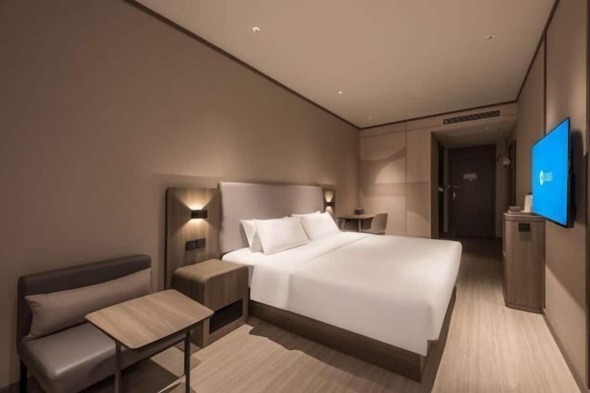 A modern hotel room with a large bed, bedside tables, a seating area, and a flat-screen TV.