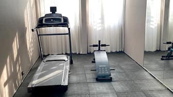 A gym with exercise equipment, including a treadmill and a bench, in a room with large windows and a mirror.