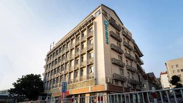 Un hôtel à plusieurs étages doté d’une architecture moderne, avec des balcons à chaque étage et une enseigne bien visible sur la façade.