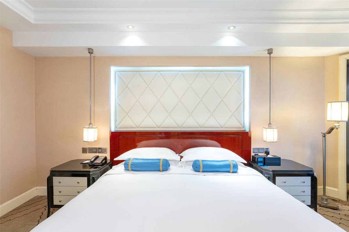 Une chambre d’hôtel avec un grand lit, deux tables de chevet, une commode, une fenêtre avec vue et un plafond doté d’un éclairage encastré.