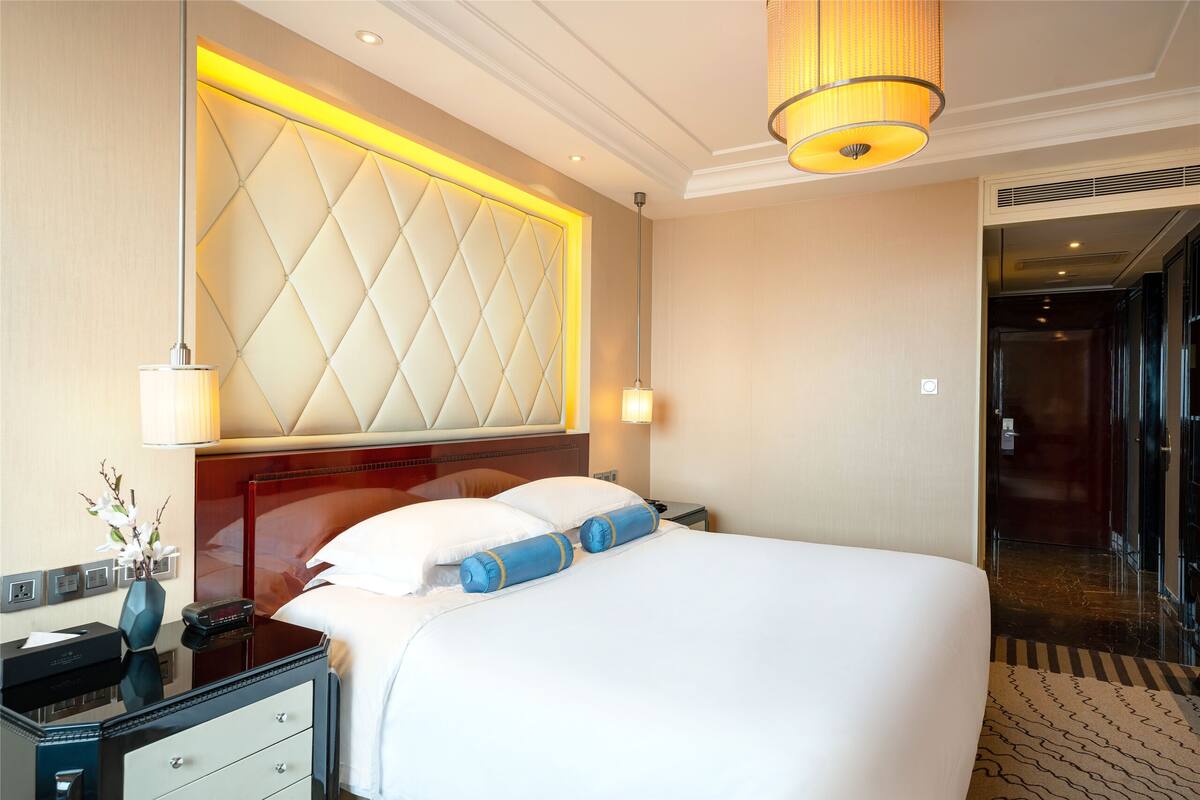 Une chambre d’hôtel avec un grand lit, une table de chevet avec une lampe et une tête de lit moderne.