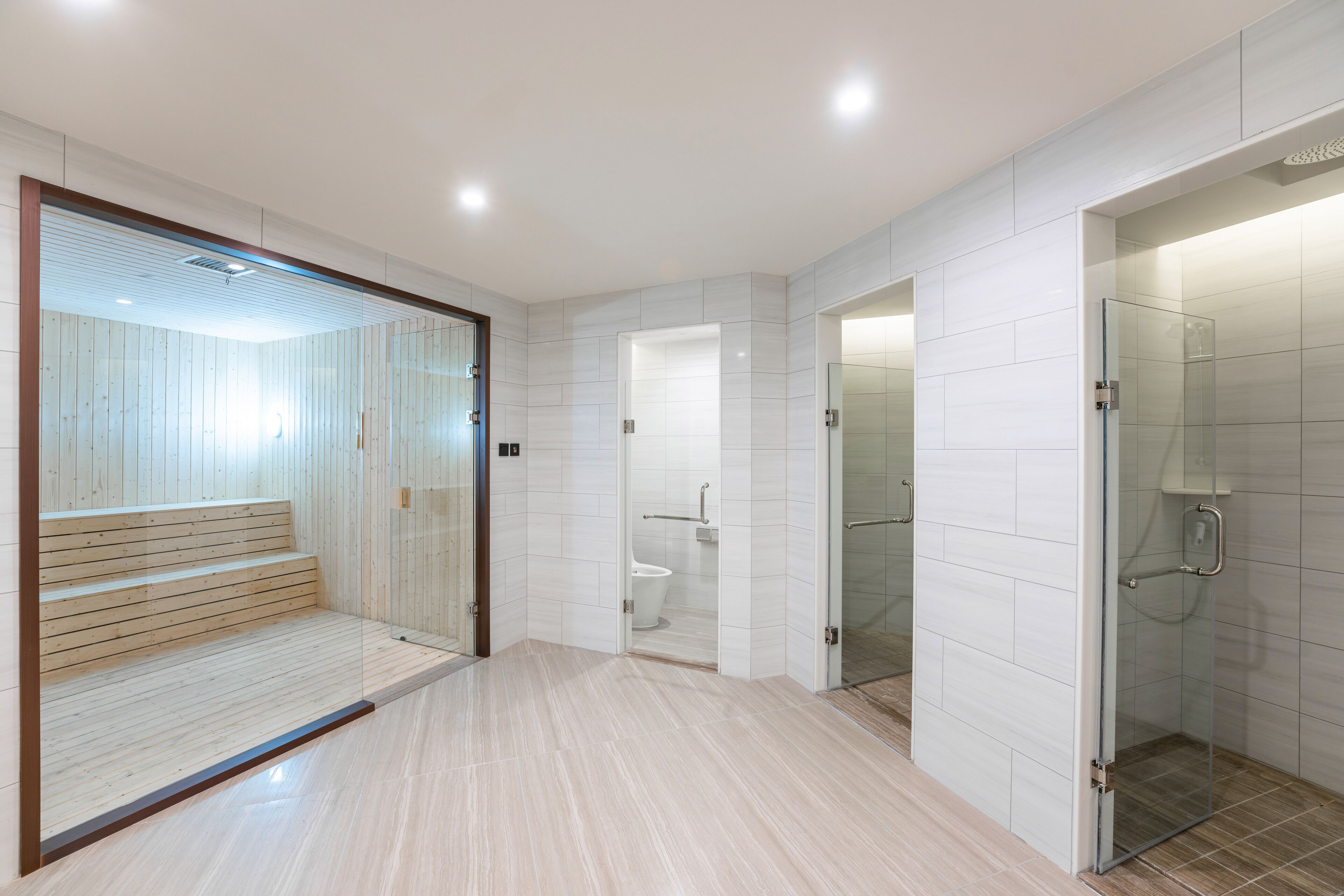 A modern bathroom with a glass shower enclosure, a wooden bench, and a toilet visible through a glass partition.