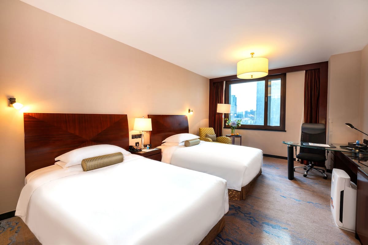Une chambre d’hôtel avec deux lits, un bureau, une chaise et une grande fenêtre donnant sur la ville.