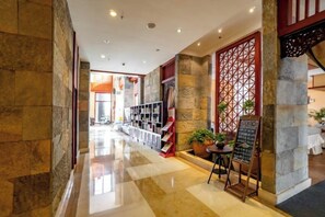 A hotel corridor with a check-in desk, a seating area with a table and chairs, and a decorative wall with a geometric pattern. - Maple Palace Hotel (Kunming)