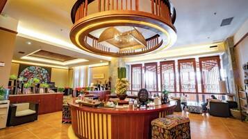 A hotel lobby with a central circular wooden structure, a reception desk, and a large window with traditional lattice design.