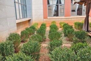 A courtyard with neatly arranged shrubs and a building with large windows and a brick facade. - Maple Palace Hotel (Kunming)