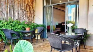 An outdoor seating area with wicker chairs and tables, surrounded by greenery and a bamboo wall. - Maple Palace Hotel (Kunming)